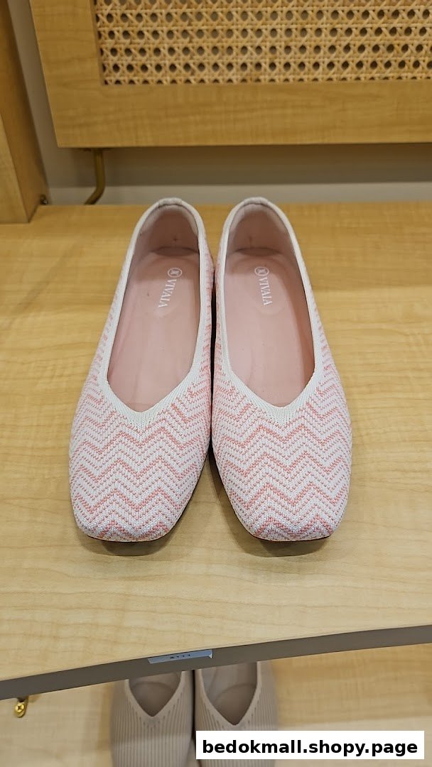 A pair of pink and white patterned flat shoes displayed on a wooden shelf.