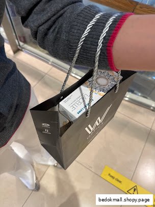 A person holds a W Optics shopping bag with a box of Lacelle contact lenses.