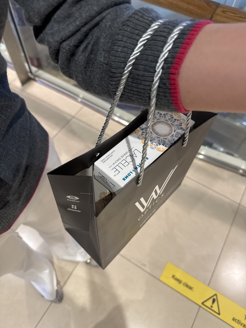 Person holding a W Optics shopping bag with contact lenses inside.