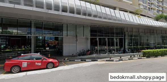 Exterior of a modern building with glass facade, parked red car, and bicycles.