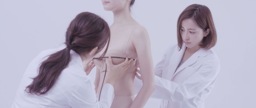 Two women measuring another woman for a bra fitting.
