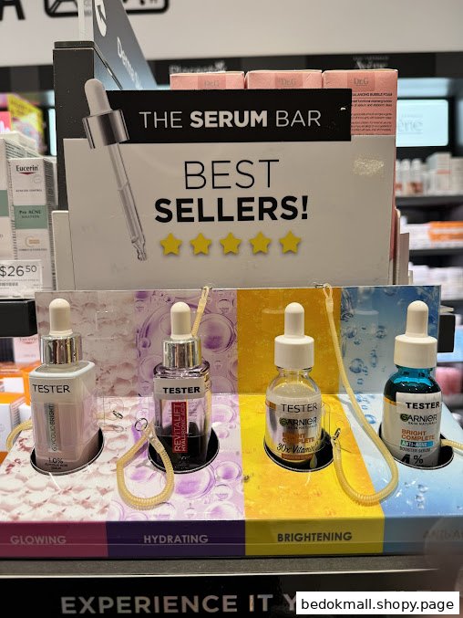 A retail display stand showcasing 'The Serum Bar Best Sellers' with tester bottles.