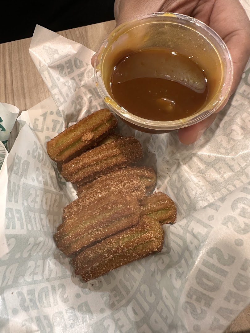 Churros with dipping sauce in a basket with branded paper.