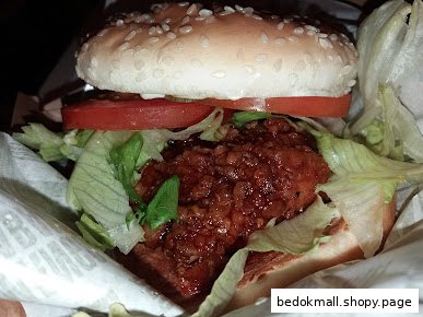 Close-up of a saucy chicken burger with lettuce and tomato in a wrapper.