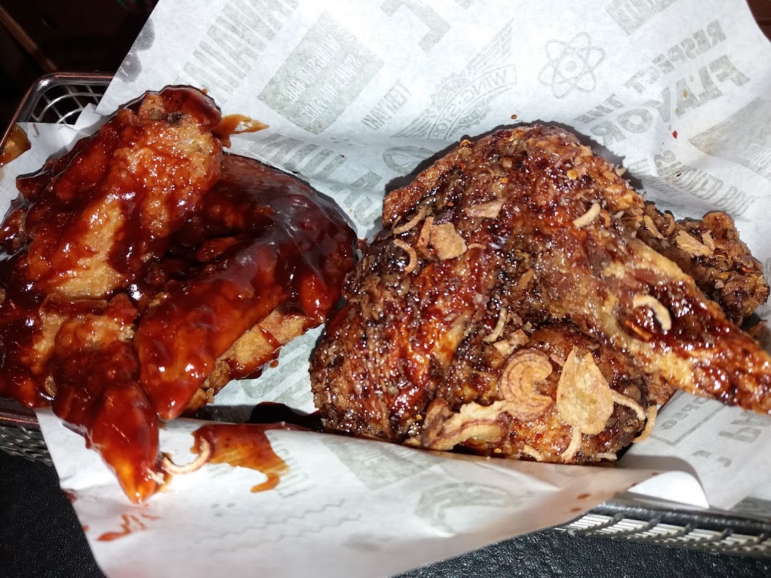Two sauced chicken wings in a basket lined with branded paper.