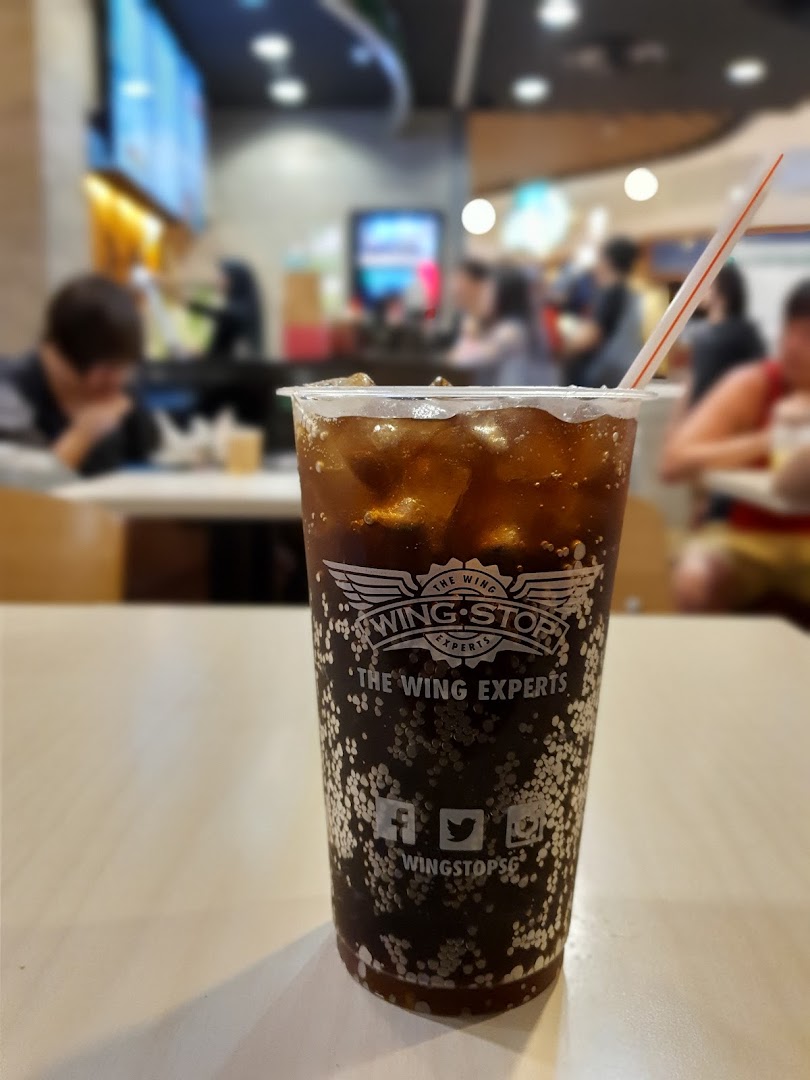 A Wingstop soda with ice and straw on a table, with blurred restaurant interior.