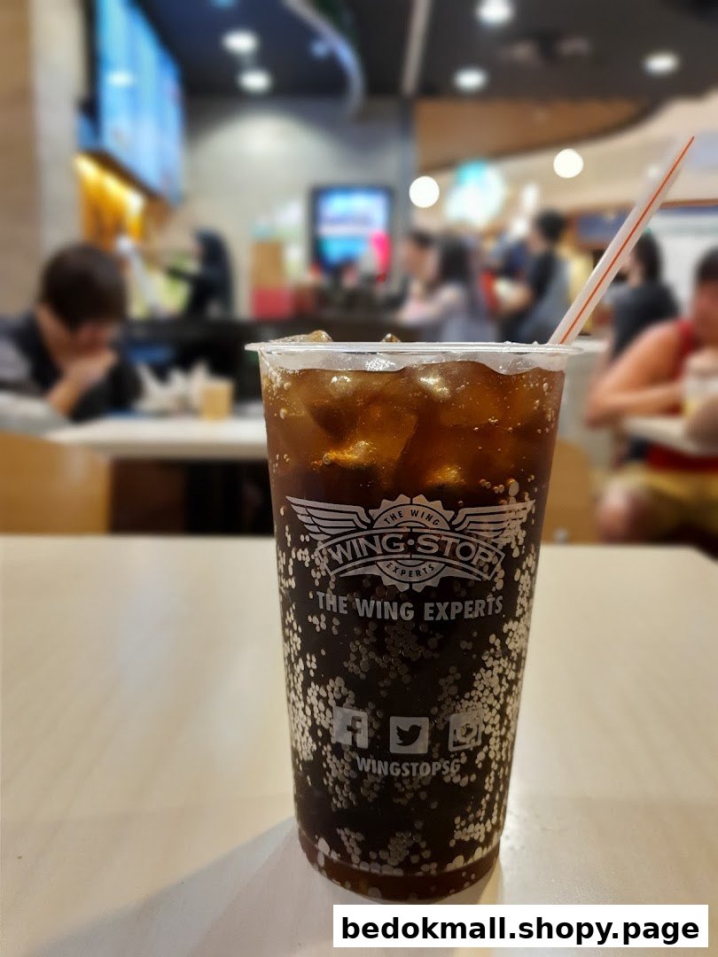 A Wingstop soda with ice and straw on a table, with blurred restaurant interior.