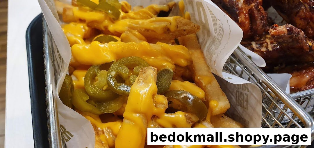 Close-up of cheese fries with jalapeños and chicken wings in a basket.