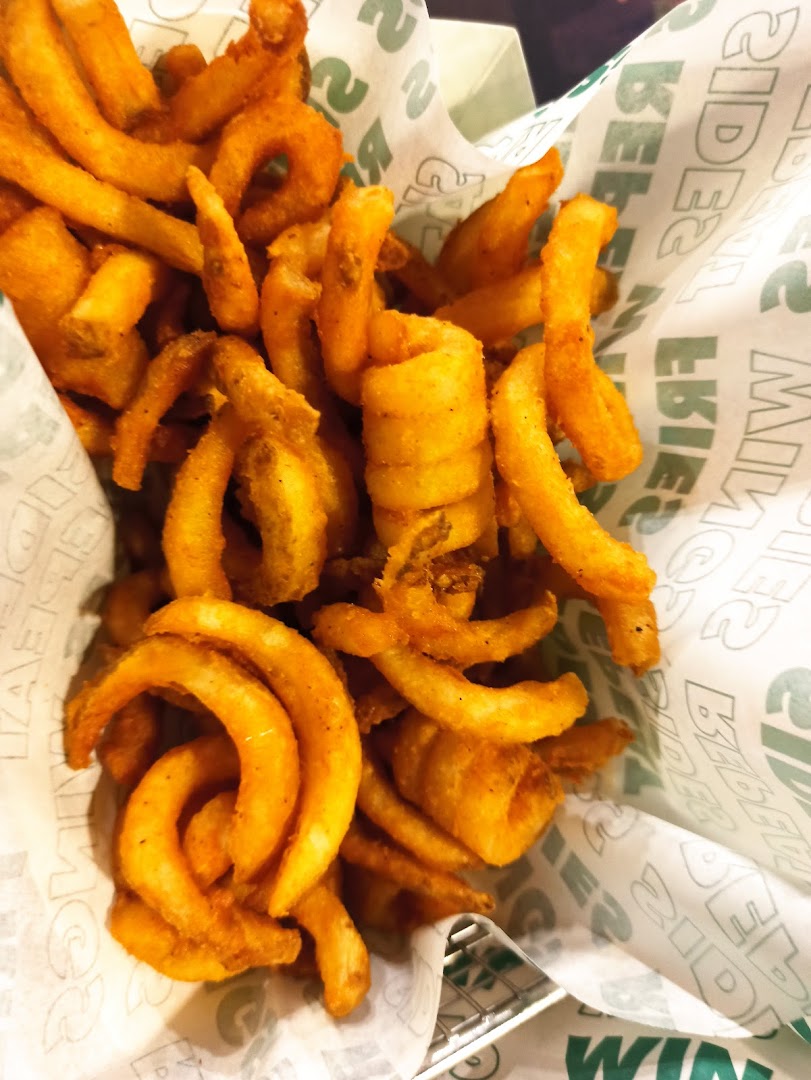 A close-up of golden curly fries in a basket with Wingstop branded paper.