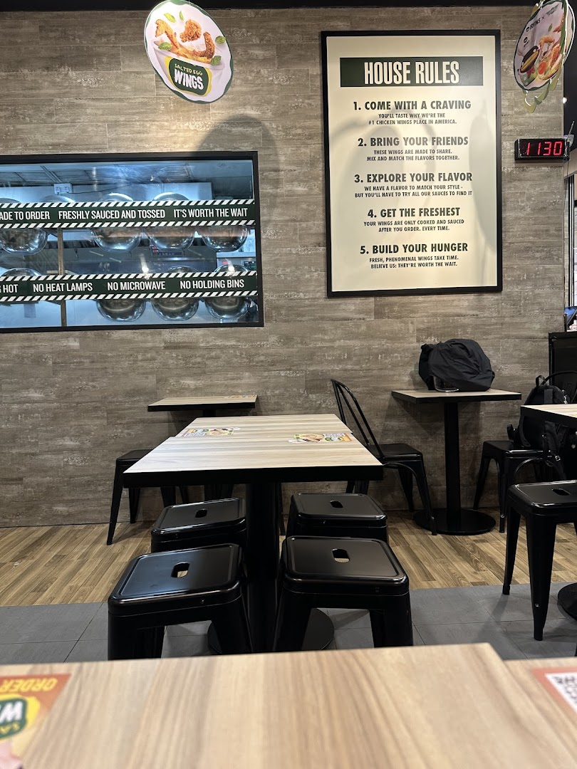 Interior view of a restaurant with tables, chairs, wall signs, and a kitchen window.
