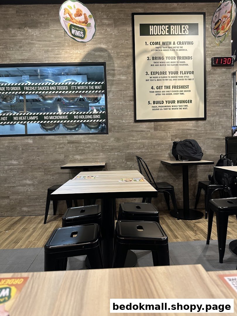 Interior view of a restaurant with tables, chairs, wall signs, and a kitchen window.
