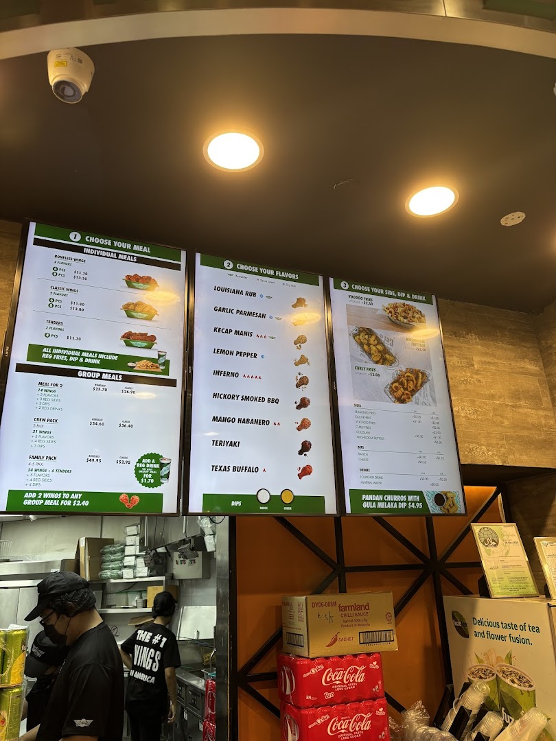 Digital menu boards, staff in a kitchen area, and stacked products inside a shop.