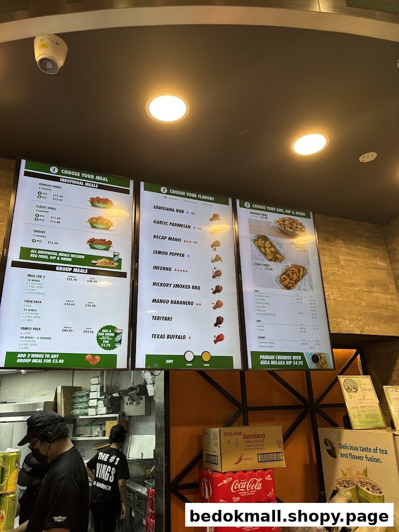 Digital menu boards, staff in a kitchen area, and stacked products inside a shop.