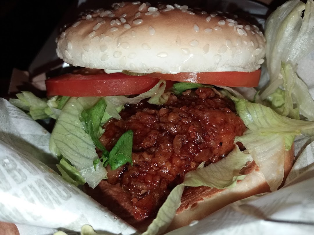 Close-up of a burger with a saucy patty, lettuce, and tomato.