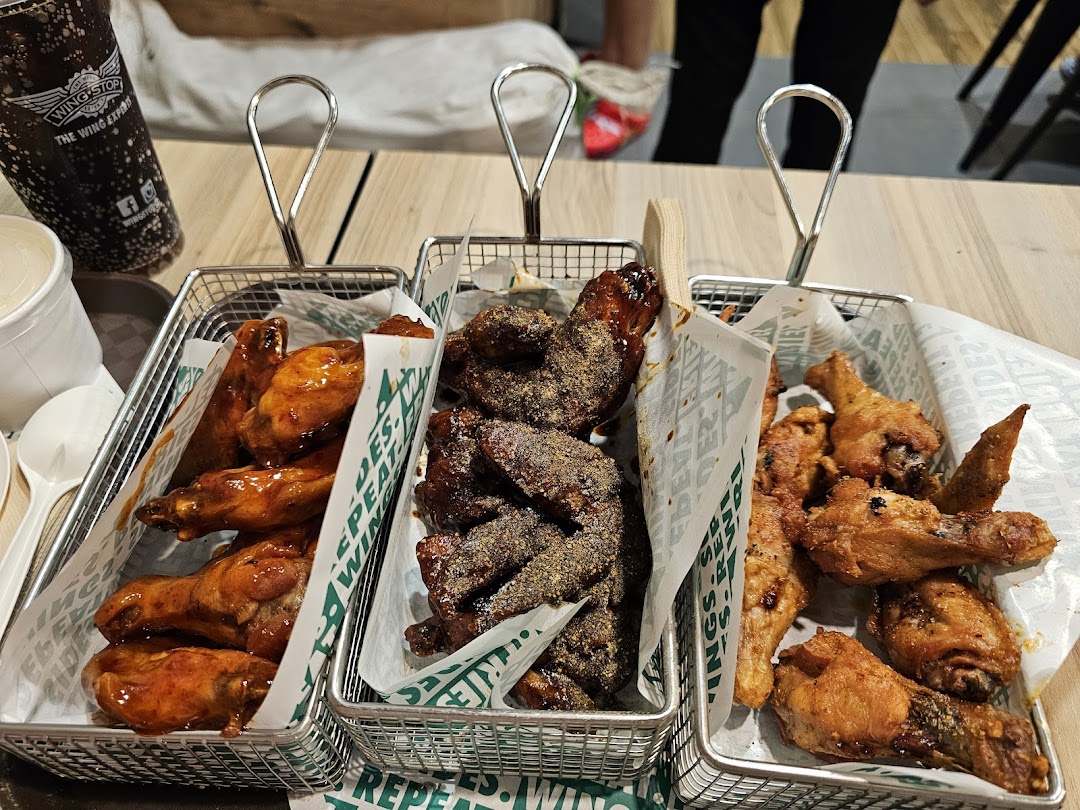 Three baskets of chicken wings and a drink on a table.