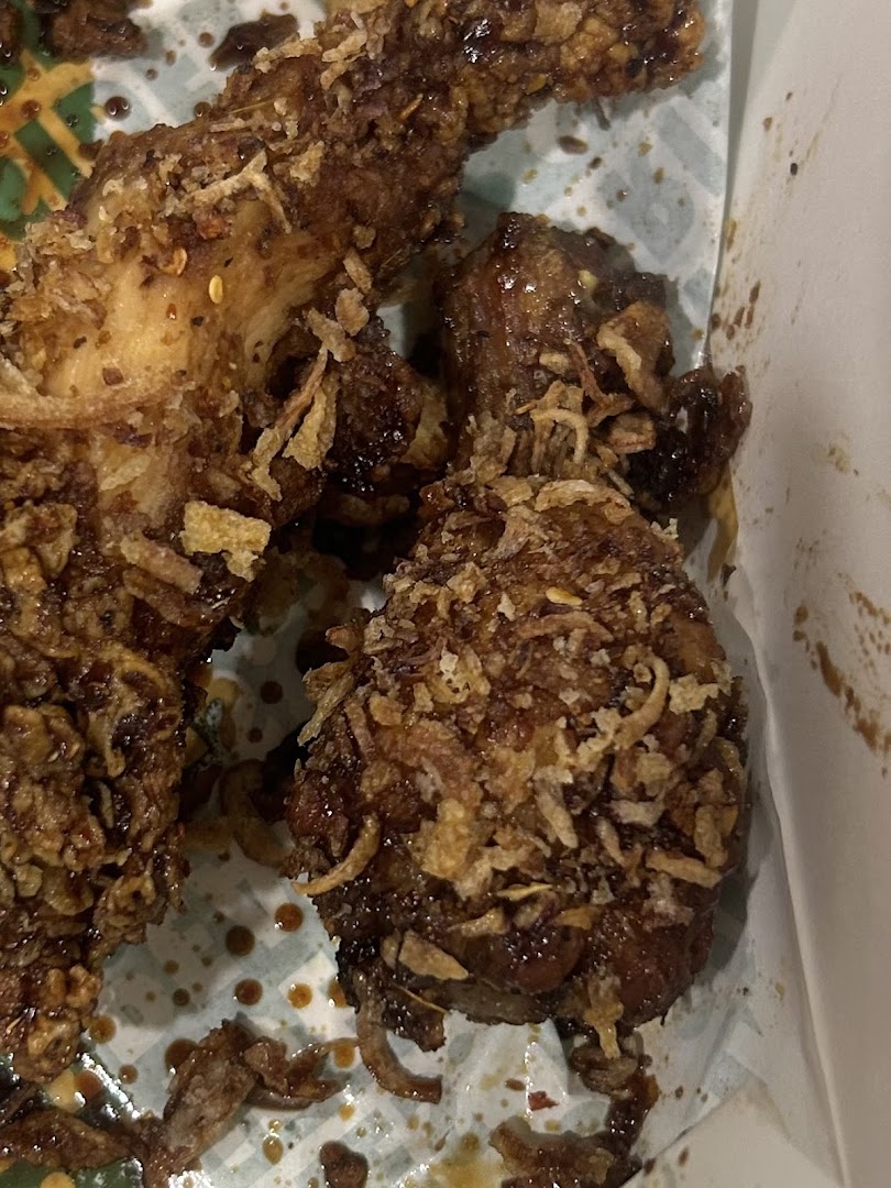 Close-up of fried chicken pieces with sauce and crispy toppings in a container.