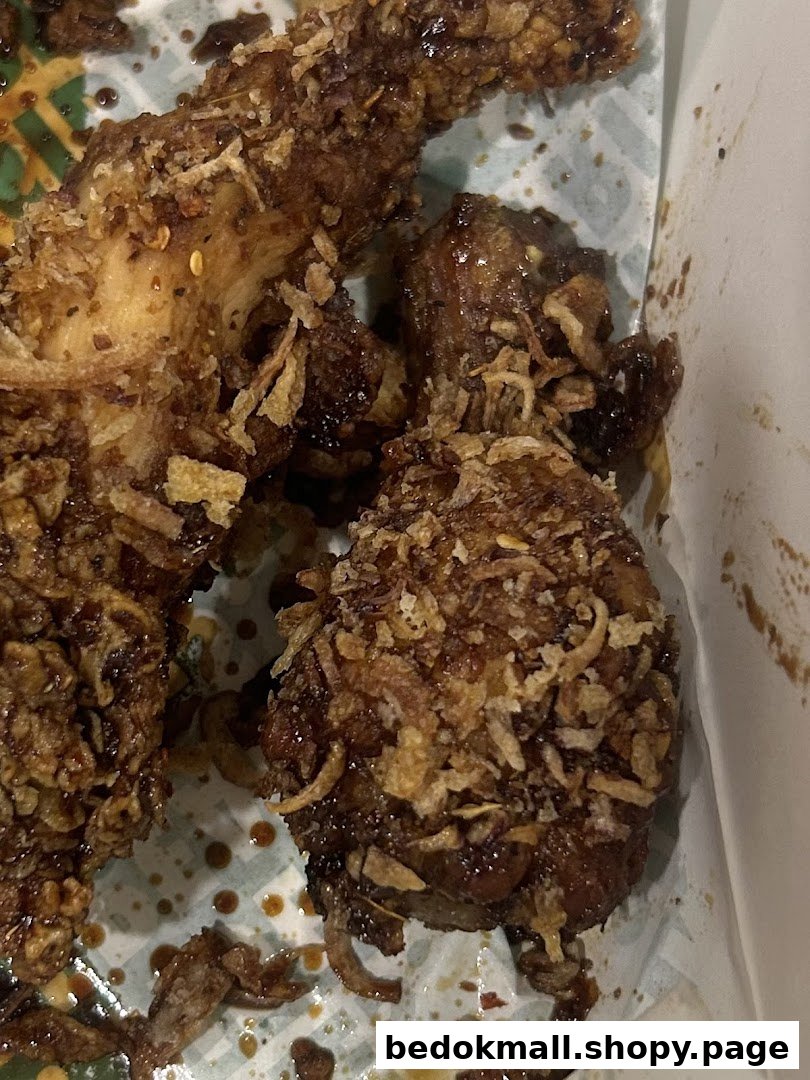 Close-up of fried chicken pieces with sauce and crispy toppings in a container.