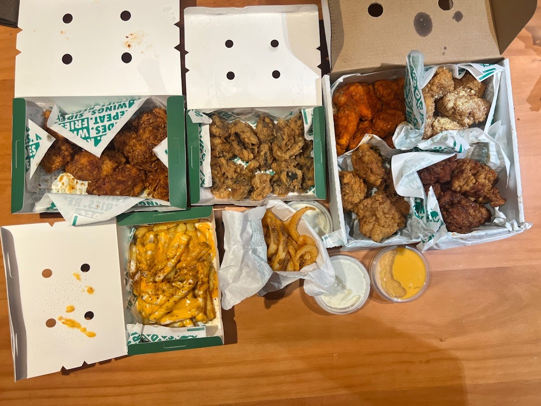 Multiple open boxes of fried chicken, fries, and sauces on a table.