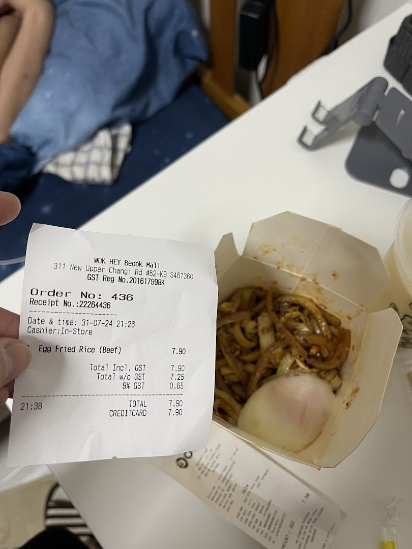A receipt from WOK HEY and a box of noodles with an egg on a table.