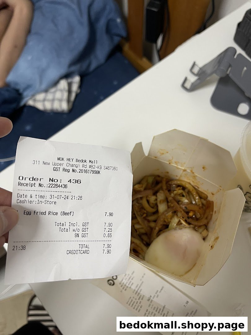A receipt from WOK HEY and a box of noodles with an egg on a table.