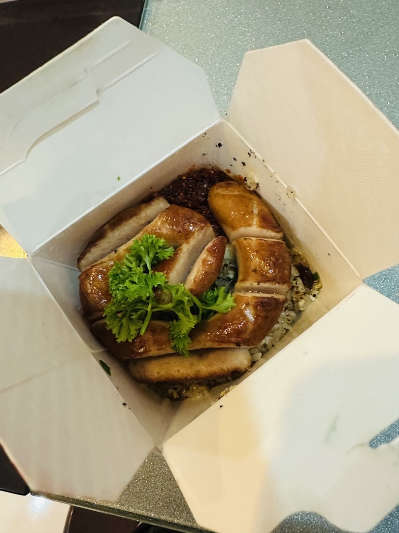 A white takeout box filled with food, topped with sliced meat and green herbs.