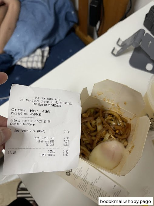 A hand holds a receipt next to an open container of noodles with an egg.
