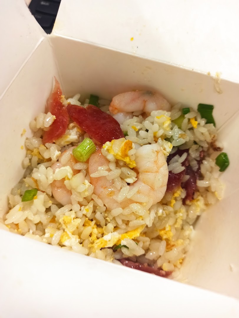Close-up of fried rice with shrimp, egg, and sausage in a takeout box.