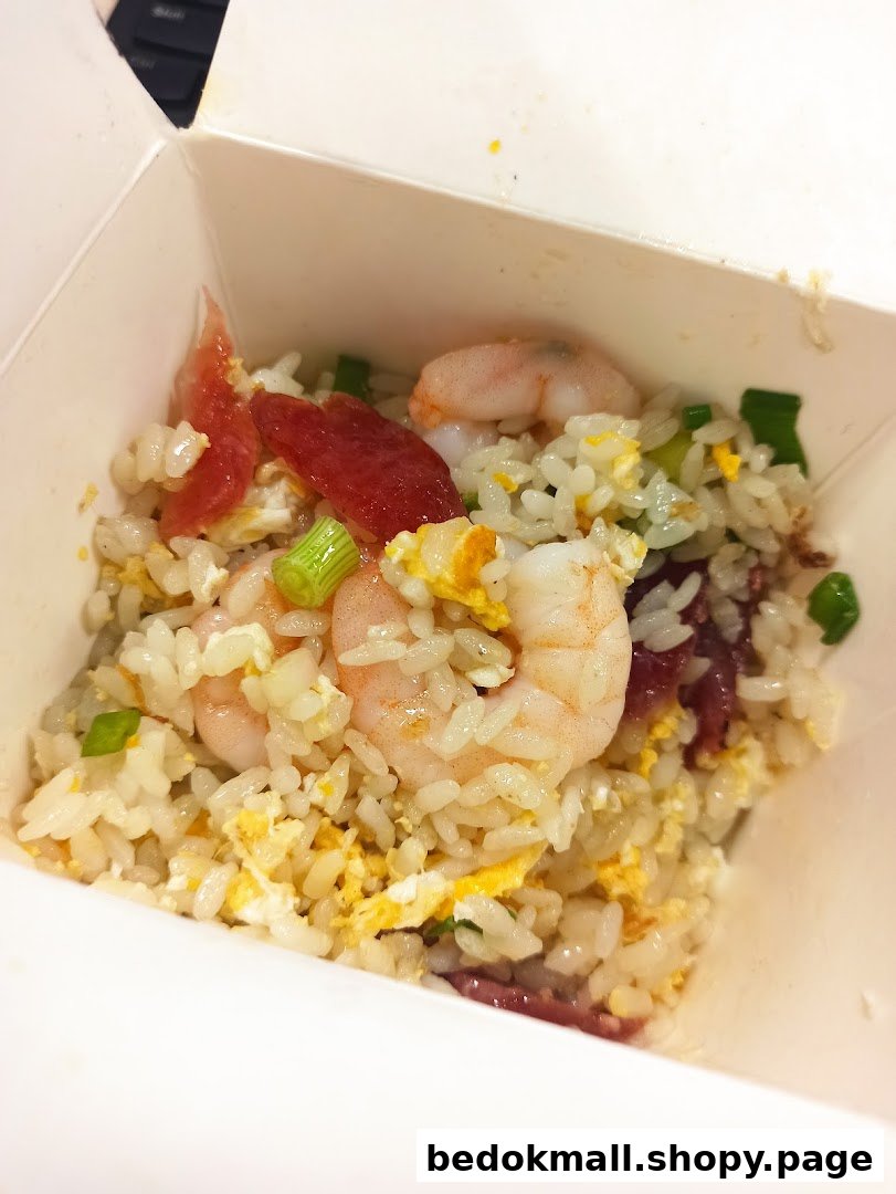 Close-up of fried rice with shrimp, egg, and sausage in a takeout box.