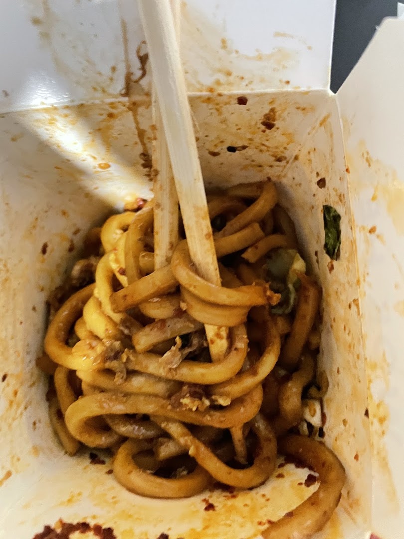 Close-up of noodles in a takeout box with chopsticks.