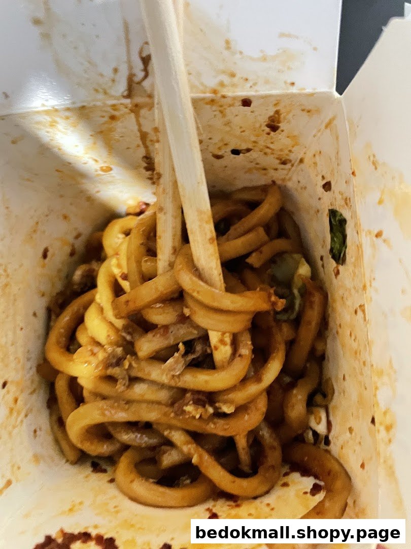 Close-up of noodles in a takeout box with chopsticks.