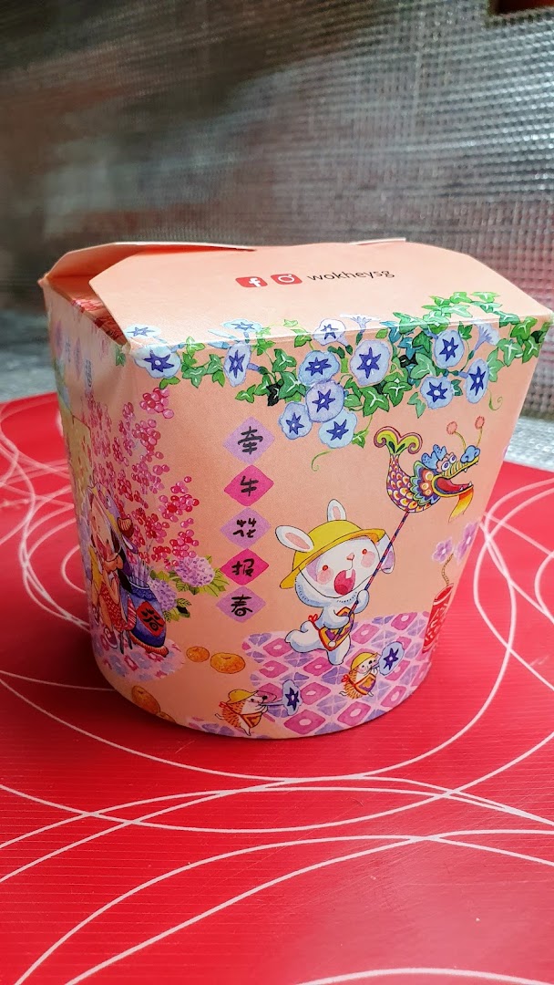A decorated WOK HEY food container with festive illustrations on a red surface.