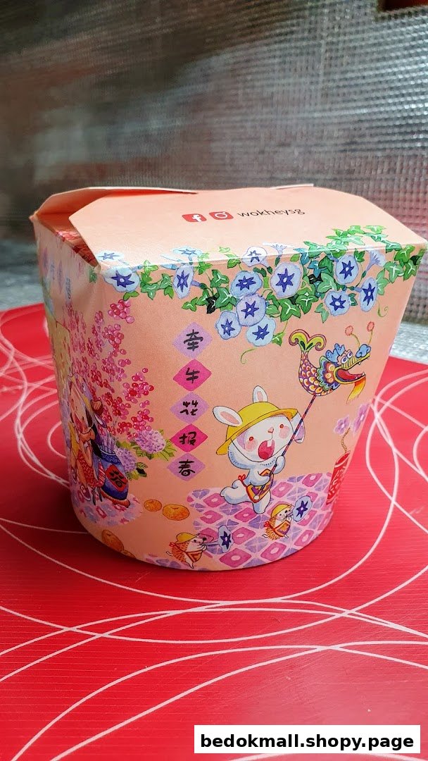 A decorated WOK HEY food container with festive illustrations on a red surface.