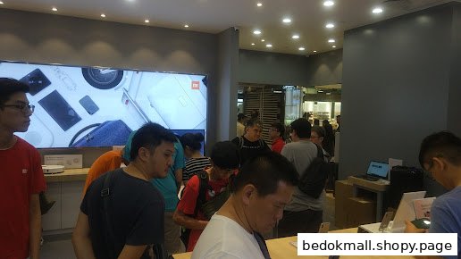 Crowded interior of a retail electronics store with customers browsing products.