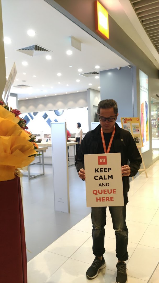 Person holding a queue sign at the entrance of a Xiaomi store.