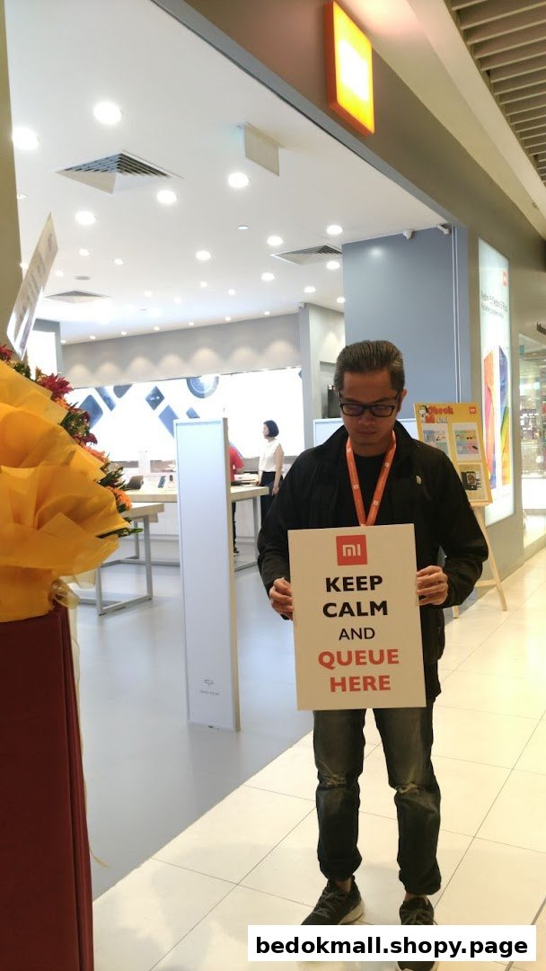 Person holding a queue sign at the entrance of a Xiaomi store.