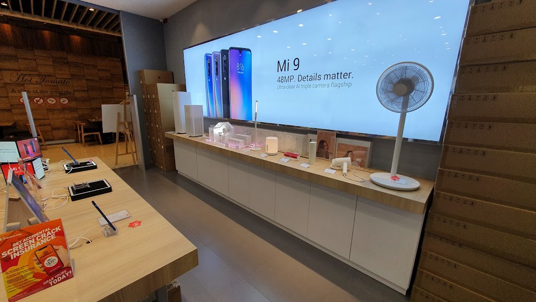 Interior of a Xiaomi store showing phones, electronics, and a large product display screen.