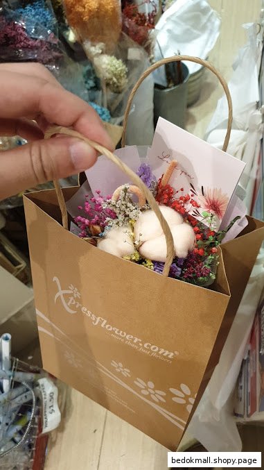 Hand holding a Xpressflower bag with a small dried flower bouquet.
