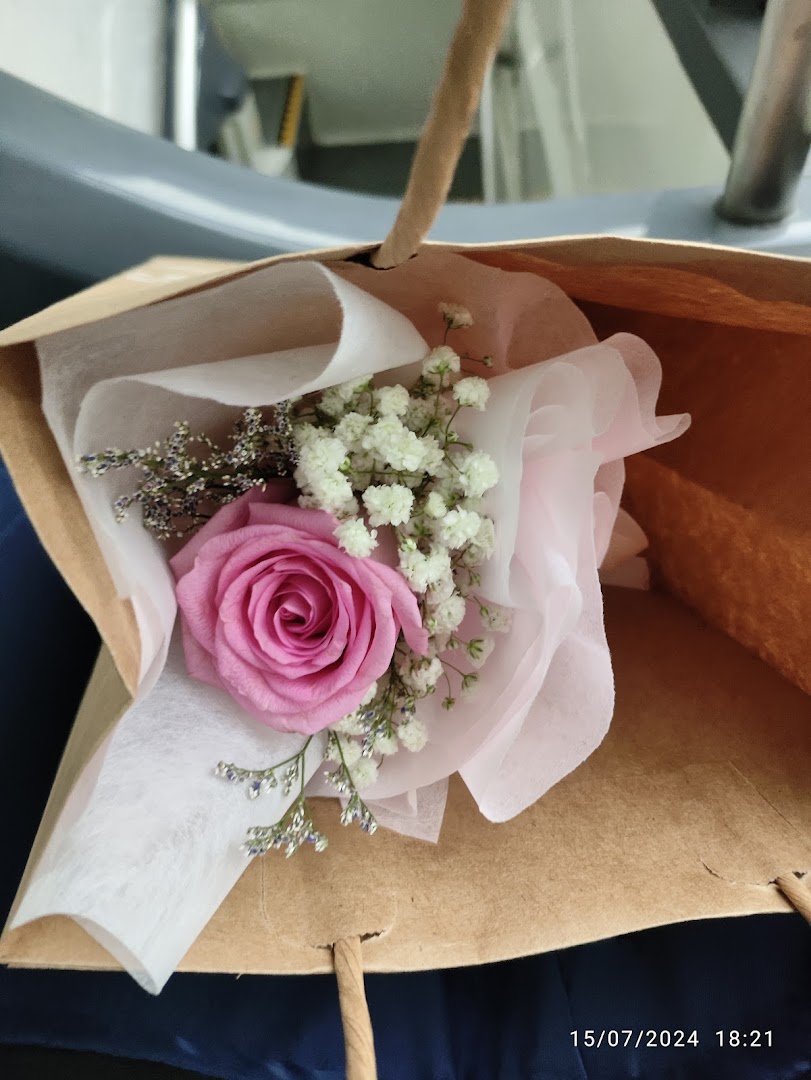 Small bouquet with a pink rose and baby's breath in a brown paper bag.