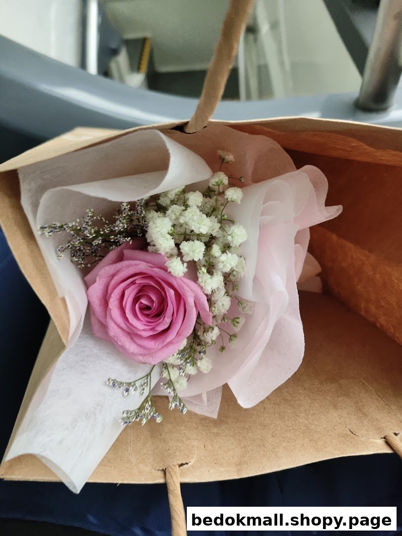 Small bouquet with a pink rose and baby's breath in a brown paper bag.