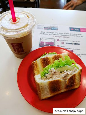 Iced coffee and a sandwich on a red plate on a white table.