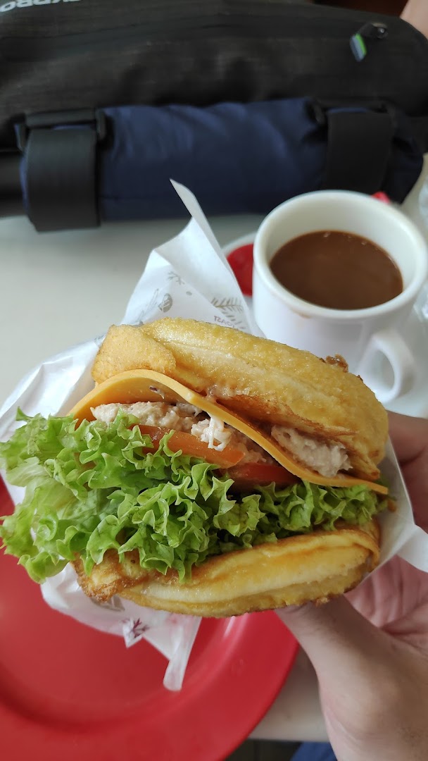 A person holding a sandwich with lettuce and cheese, next to a cup of coffee.
