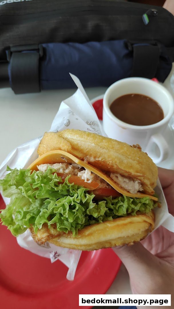 A person holding a sandwich with lettuce and cheese, next to a cup of coffee.