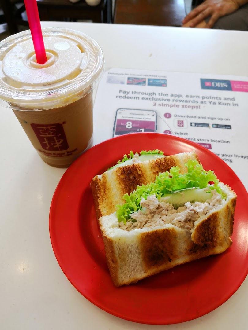 A tuna sandwich and iced coffee on a red plate at a table.