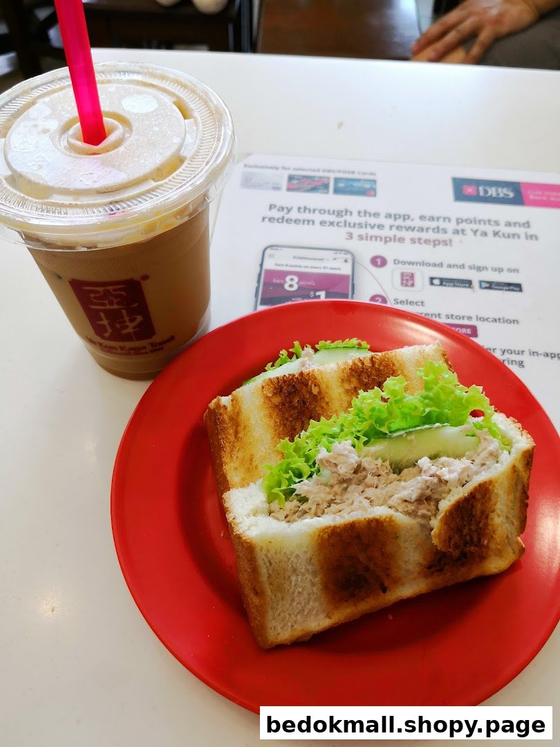 A tuna sandwich and iced coffee on a red plate at a table.