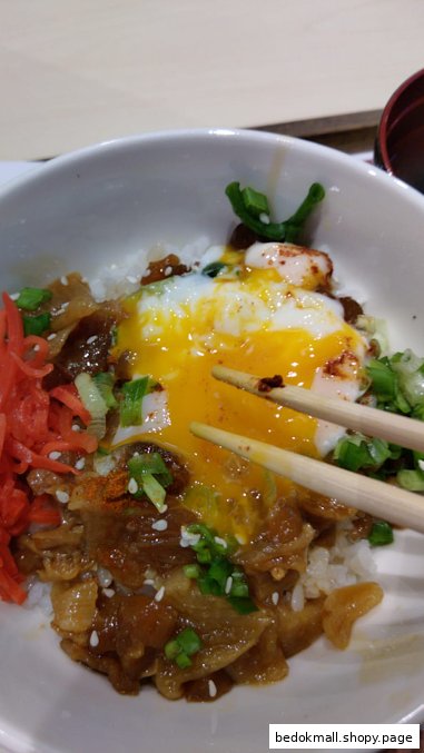 Close-up of a bowl of beef and rice with a runny egg and chopsticks.