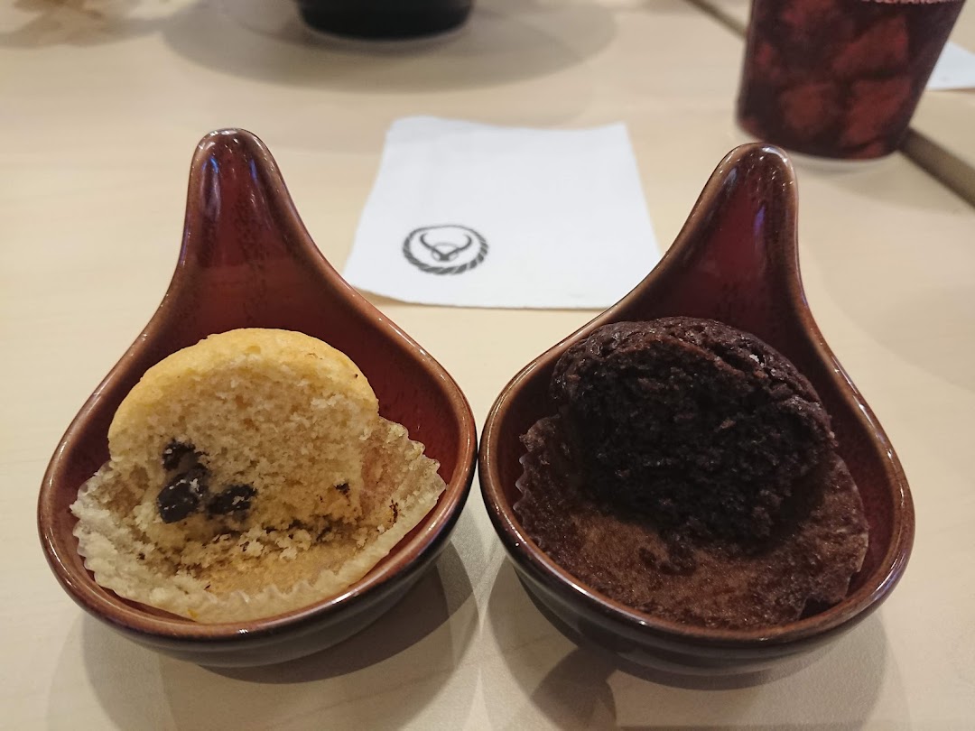 Two mini muffins in small dishes on a table with a napkin.