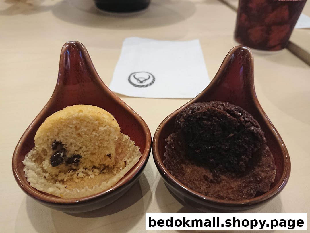 Two mini muffins in small dishes on a table with a napkin.