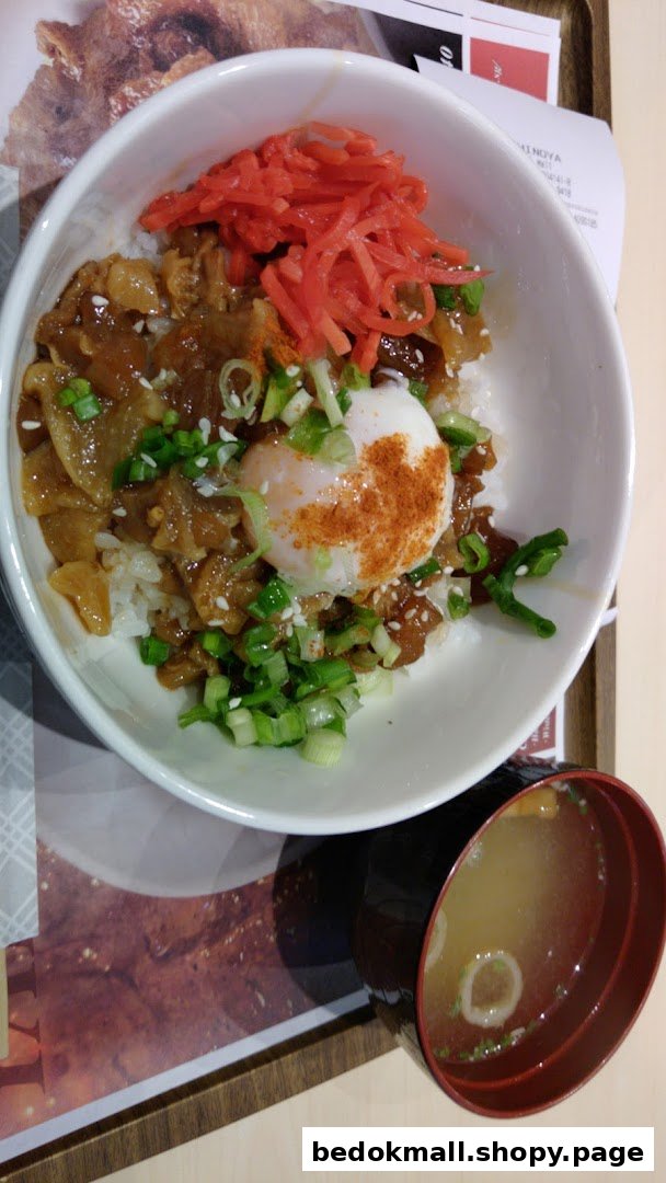 A bowl of donburi with meat, egg, and red ginger, served with miso soup.