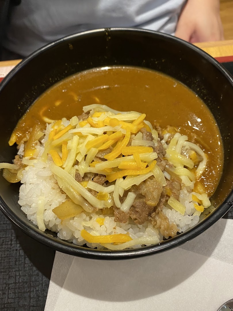 A close-up of a bowl of rice with beef, cheese, and curry sauce.