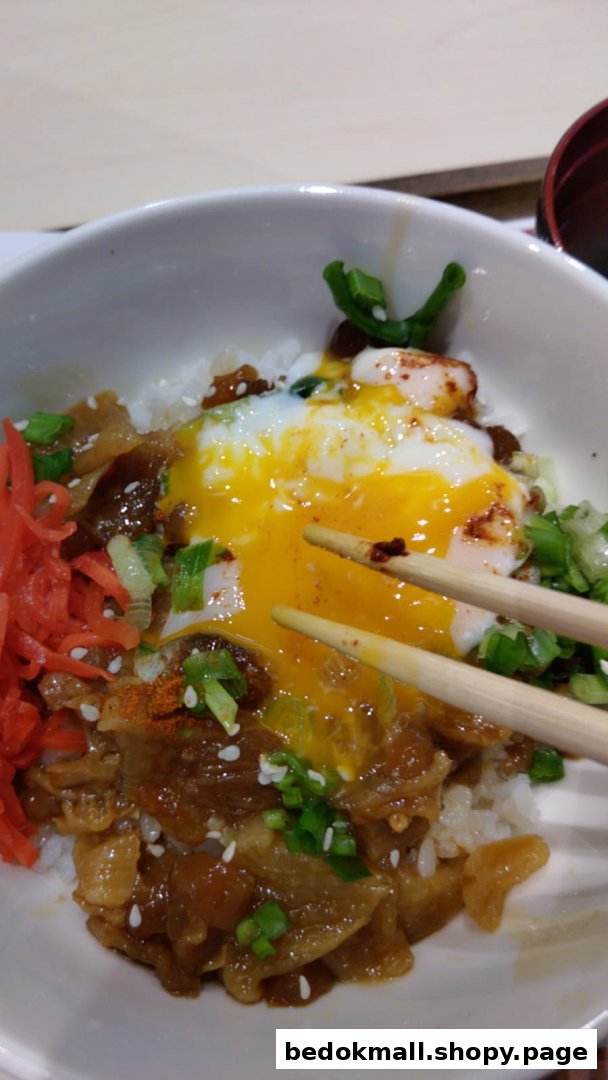 Close-up of a rice bowl with meat, runny egg, and chopsticks.